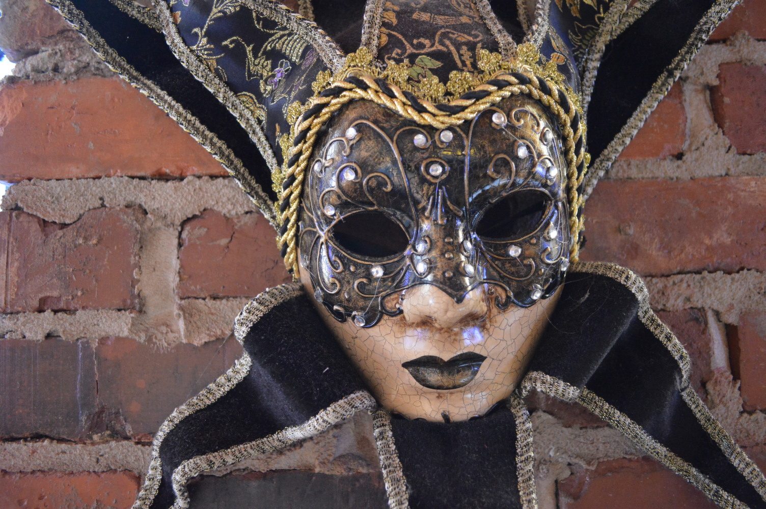 Black and gold Mardi Gras mask on an exposed brick wall